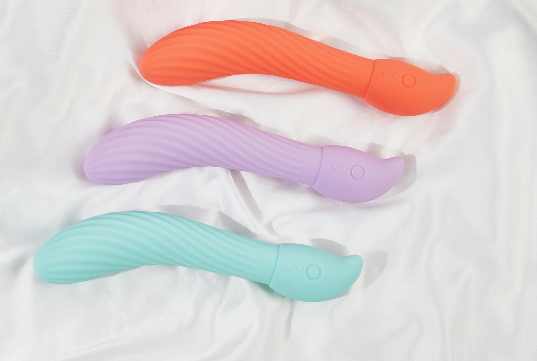 Three colorful clitoral vibrators arranged on white fabric, showing different textures and designs.