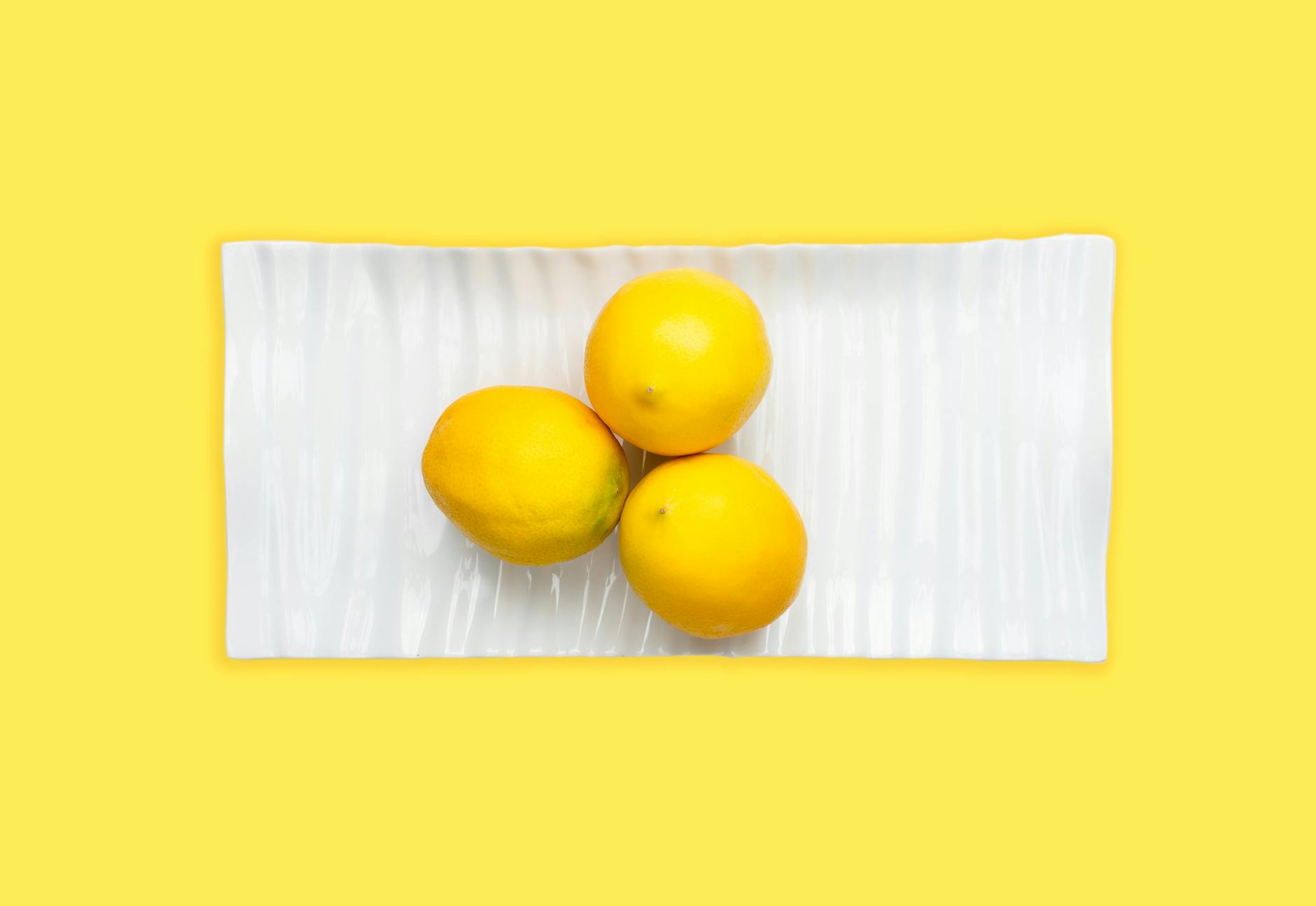 Hand holding a fresh lemon against a vibrant yellow background, symbolizing freshness and citrus vitality.