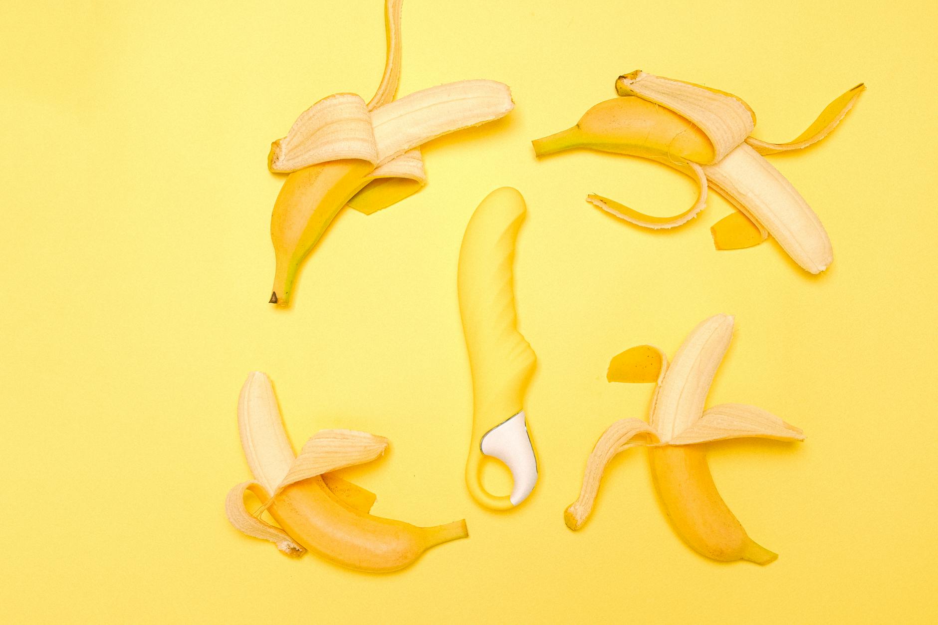 Yellow silicone lemon clitoral vibrator surrounded by fresh lemons on a bright yellow background