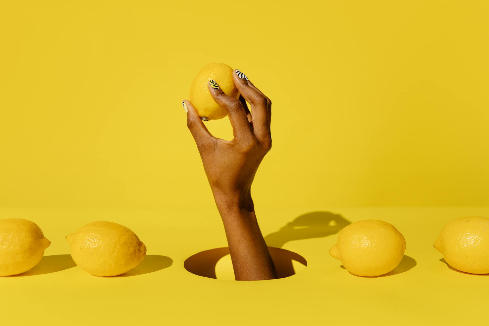 Lemon vibrator on bright yellow background surrounded by fresh lemons and flowers