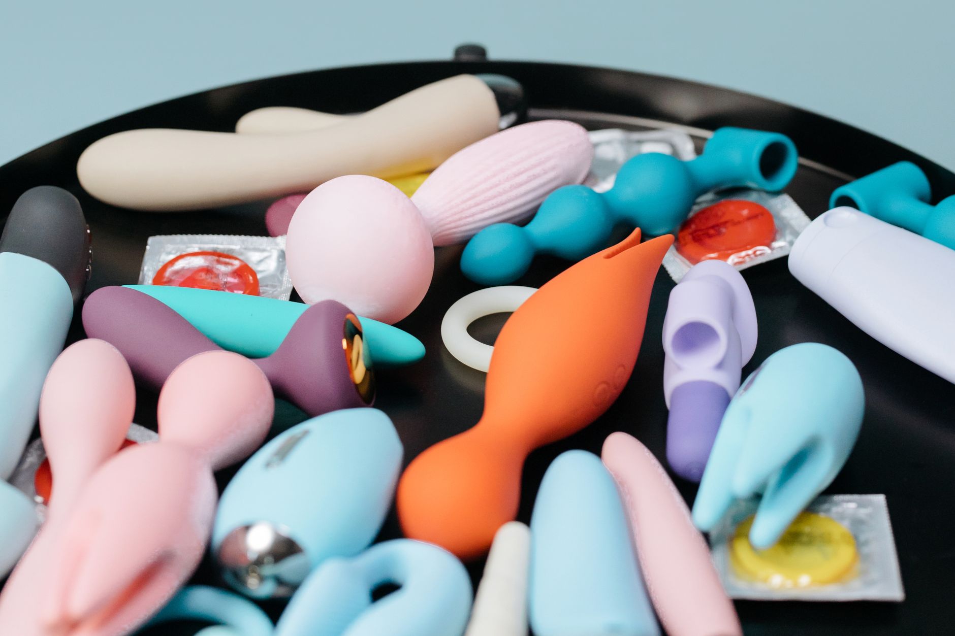 Two hands holding pink and blue silicone vibrators against a pastel background.