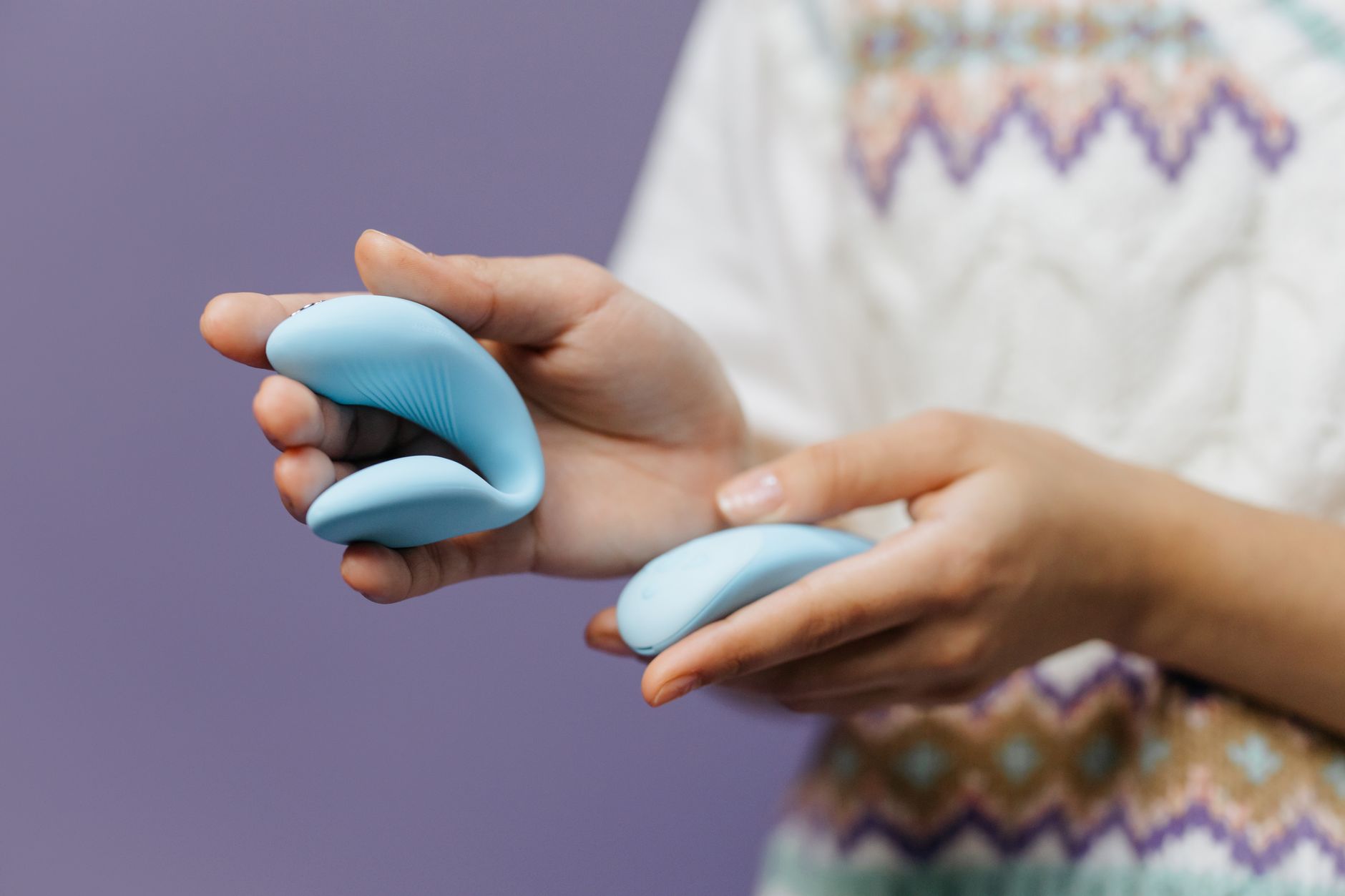 Close-up of a hand holding a sleek blue vibrator against a purple background.