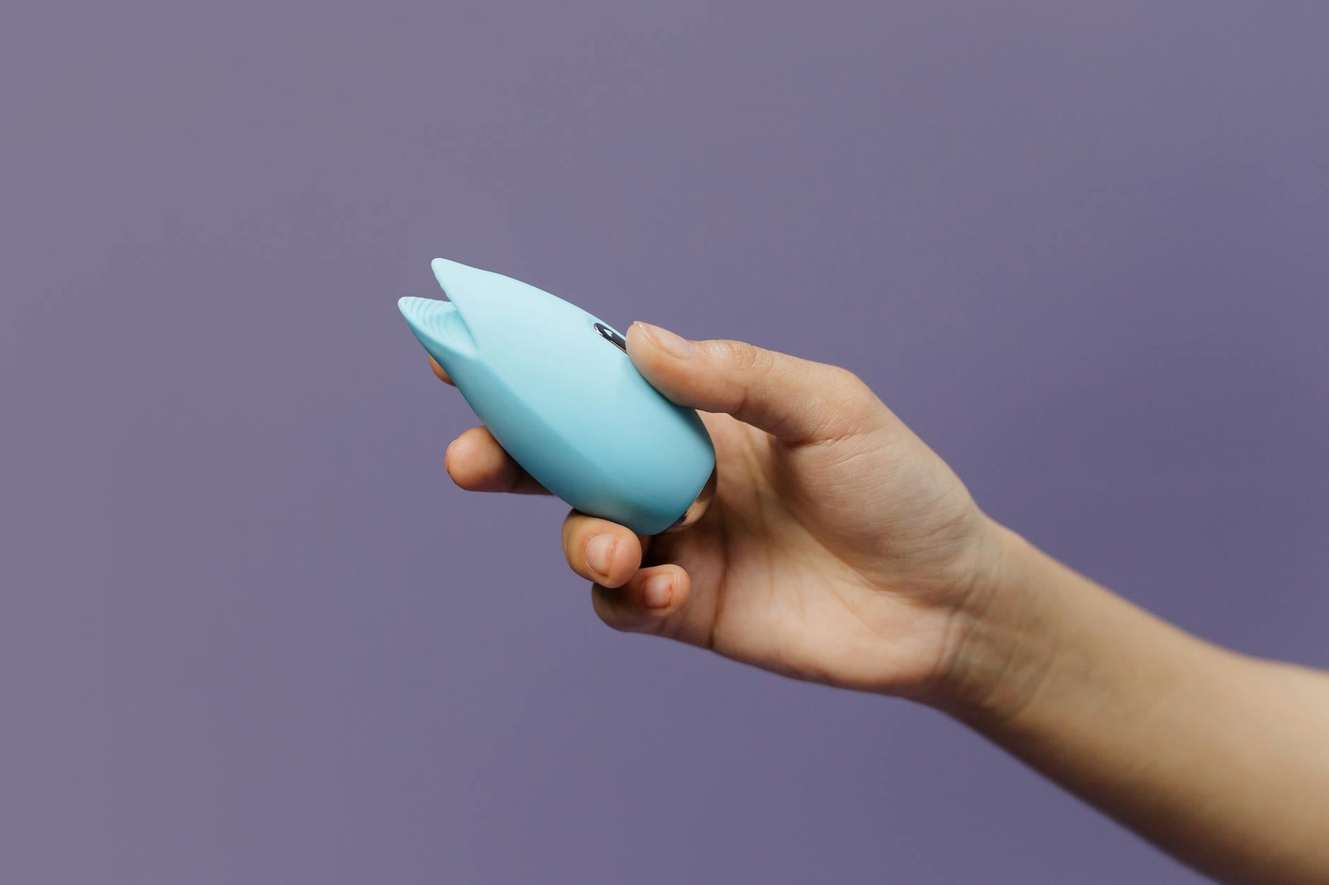 A silicone clitoral vibrator held in hand against a purple background, representing self-care during stress.