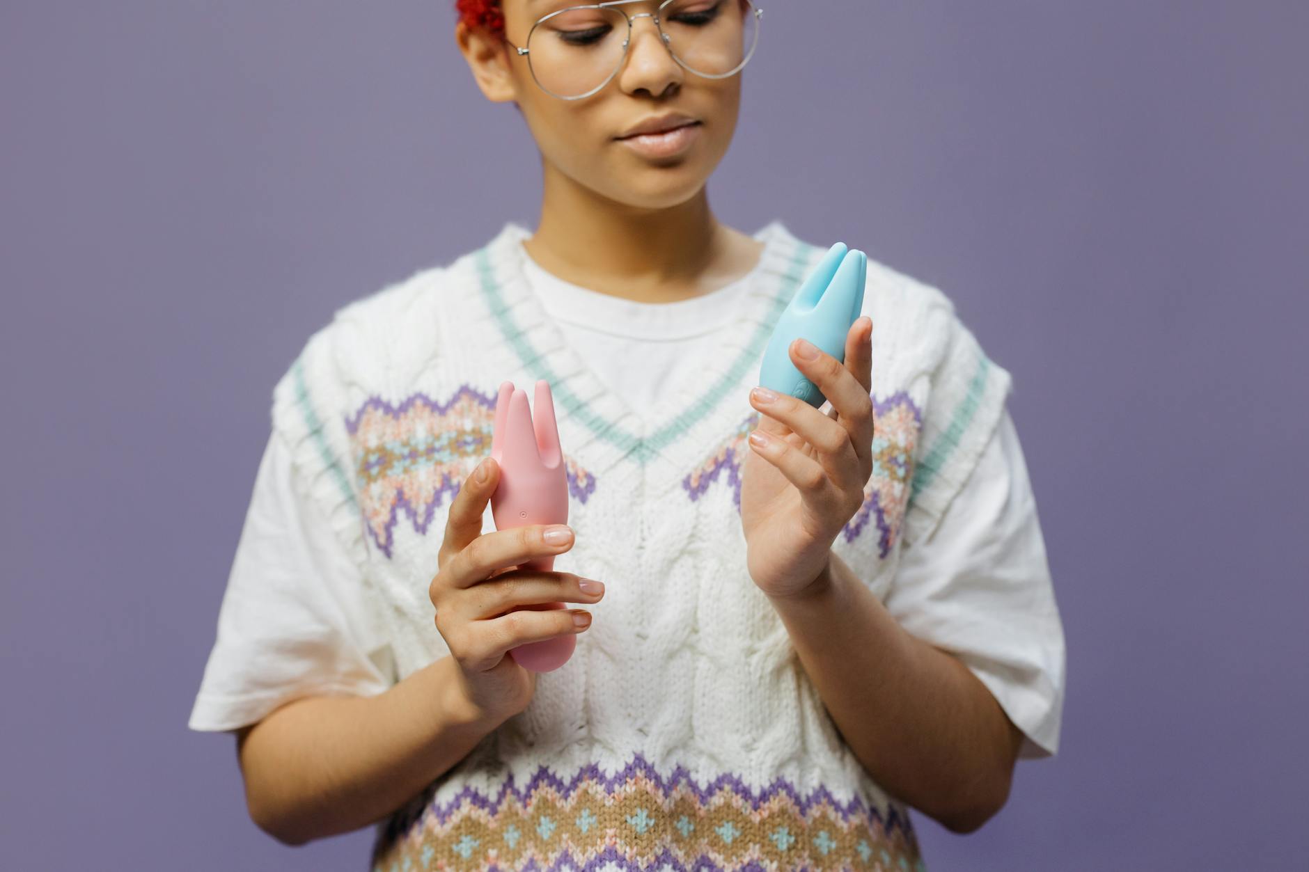 Woman holding blue and pink silicone vibrators in a thoughtful pose