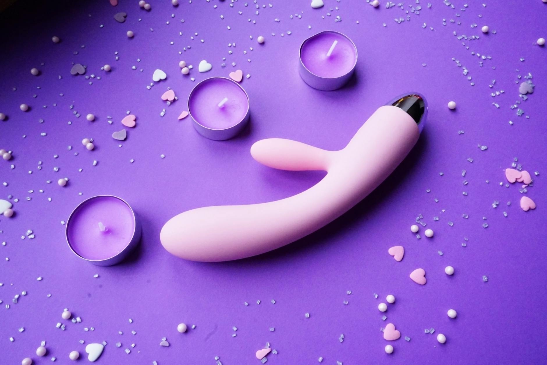 Pink vibrator on purple background with heart confetti and candles symbolizing solo pleasure and self-care after breakup